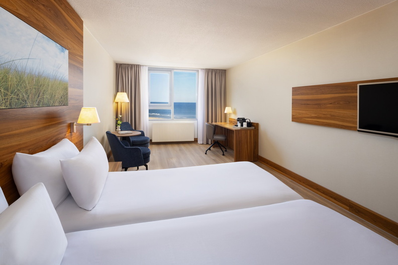 NH_Zandvoort_Rooms_Standard_Seaview_Twin_Bed_Blue_Chairs_Curtains_Open_Flowers_Desk_Coffee_Machine_TV.jpg