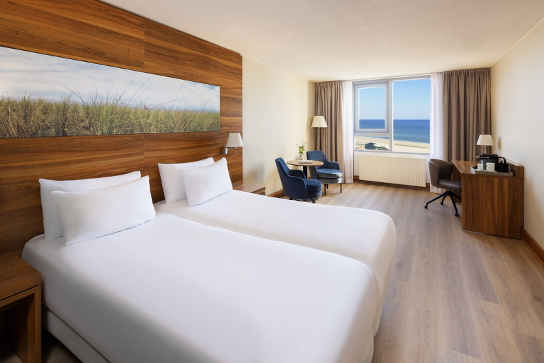 NH_Zandvoort_Rooms_Standard_Seaview_Twin_Bed_Blue_Chairs_Curtains_Open_Flowers_Desk_Coffee_Machine.jpg
