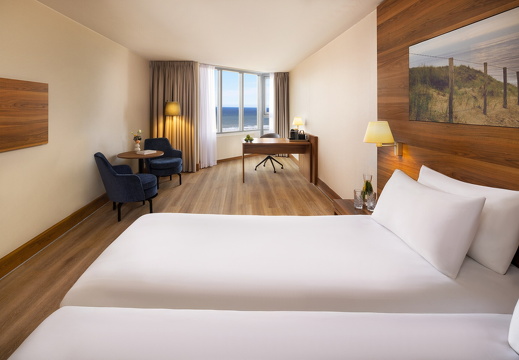 NH Zandvoort Rooms Superior Seaview Twin Bed Blue Chairs Curtains Open Flowers Desk Coffee Machine TV Water On Bedside Book